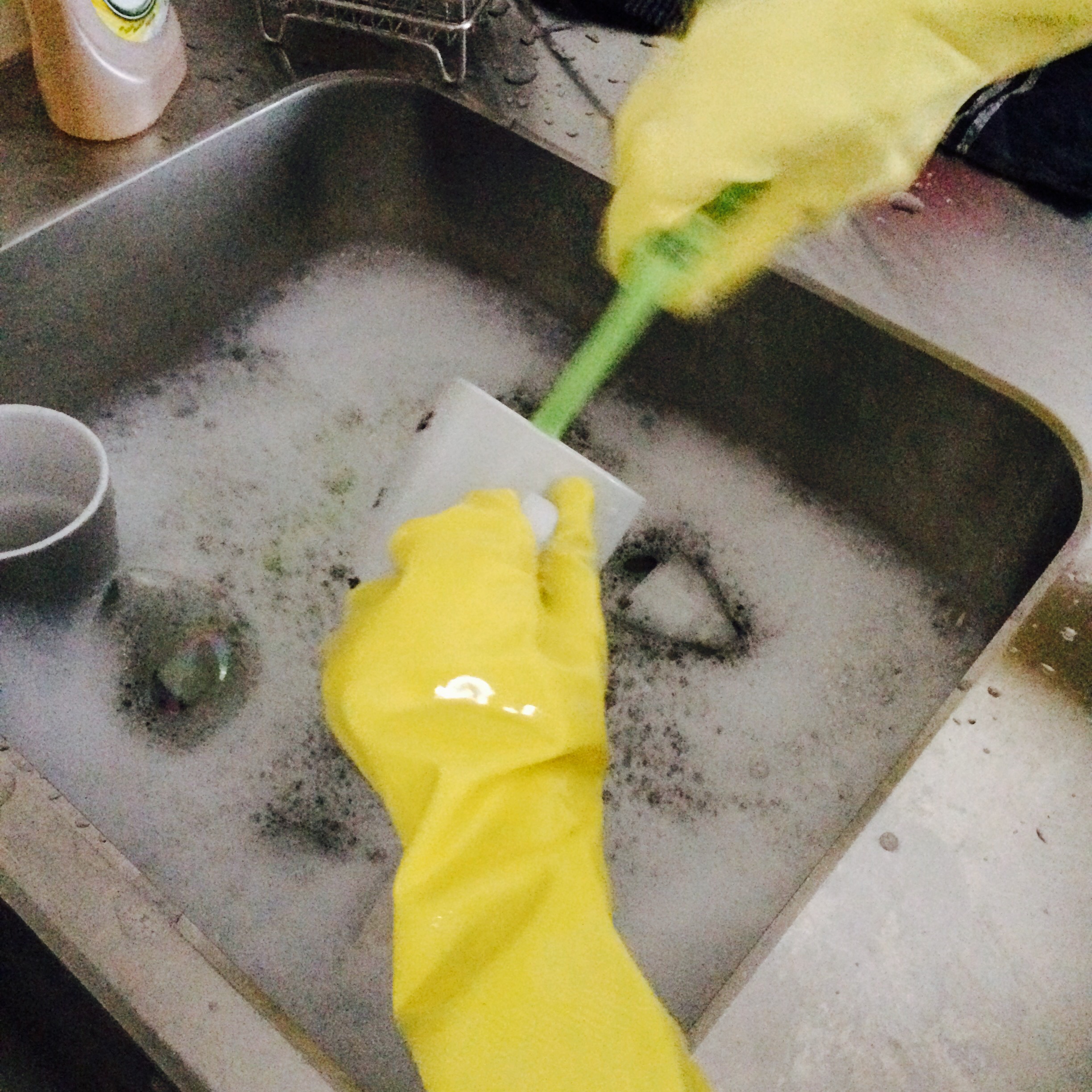två barnhänder med gula diskhandskar diskar en mugg med en grön diskborste.